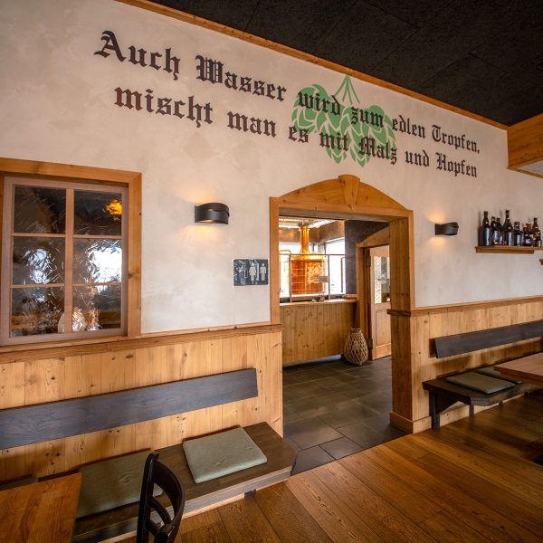Restaurant mit Sitzecken und Spruch auf der Wand "Auch Wasser wird zum edlen Tropfen, mischt man es mit Malz und Hopfen"