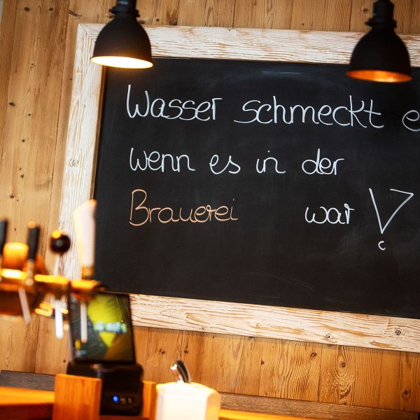 Tafelschild mit Spruch "Wasser schmeckt erst, wenn es in der Brauerei war" vor der Zapfanlage